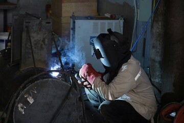 professional welder is welding metal frame and bright sparks in a workshop