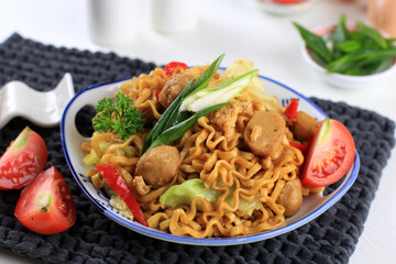 Mie goreng or Stir Fried Egg Noodles is Traditional Indonesian Food with Chicken, Egg, Tomato, Onion, Vegetable and Sweet Soy Sauce in White Plate Served on Wooden White Table. Top View.