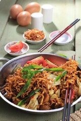 Chinese Style Mie Goreng or Stir Fried Egg Noodles is Traditional Indonesian Food with Chicken, Egg, Tomato, Onion, Vegetable and Sweet Soy Sauce in White Plate Served on Wooden White Table.