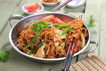 Chinese Style Mie Goreng or Stir Fried Egg Noodles is Traditional Indonesian Food with Chicken, Egg, Tomato, Onion, Vegetable and Sweet Soy Sauce in White Plate Served on Wooden White Table.