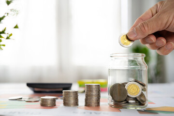 Saving coins, money. Hand of business man putting coins in glass bottle with stack coin