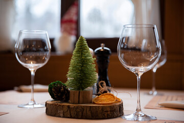 Stroik świąteczny na stole restauracyjnym. Lampki wina czekają na klientów. W tle duże okno ze świątecznym elfem na parapecie. Wystrój restauracji z okazji Bożego Nardzenia.