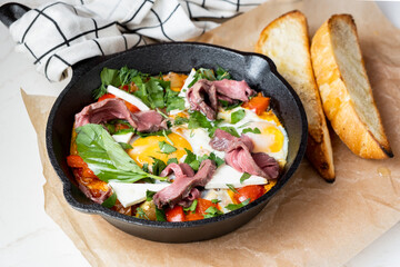 Fried eggs in a pan with meat, vegetables and herbs.