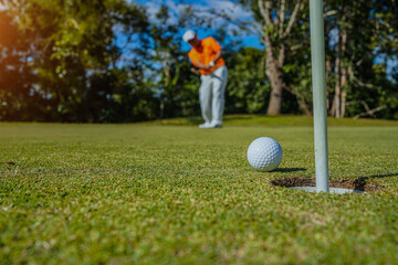 Golfer putting ball on the green golf, lens flare on sun set evening time. Golfer action to win after long putting golf ball in to the hole