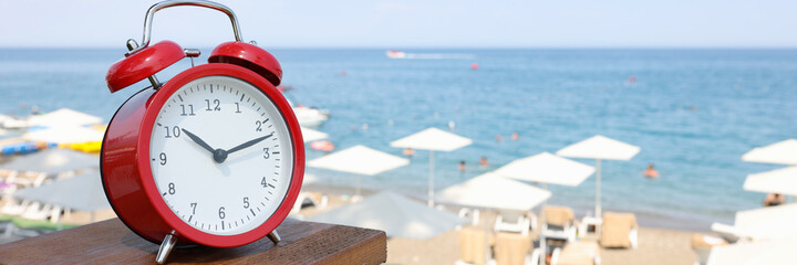 Red alarm clock standing on sea beach of hotel closeup