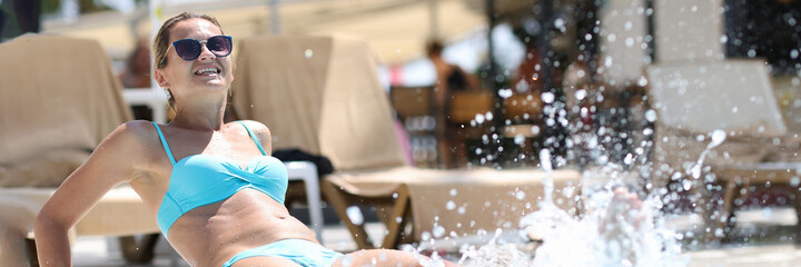 Young woman sitting on edge pool and splashing water with her feet