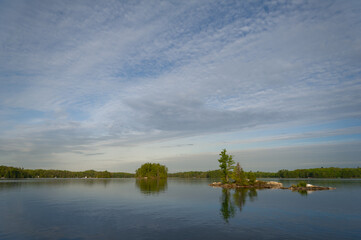 Landscape panorama of a calm lake in the Kawarthas, Ontario Cottage Country. Cottages nestled among green trees are visible across the blue waters.