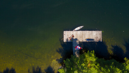 Aerial view of a cottage wooden pier on a lake in Muskoka, Ontario Canada. Two brown Adirondack...