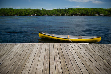 Yellow canoe tied to a wooden dock in Muskoka, Ontario Canada. Cottages are visible in background...