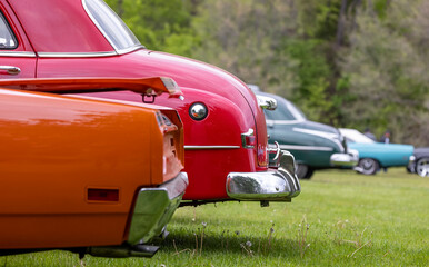 Tail end of several classic cars parked in the grass, with selective focus.