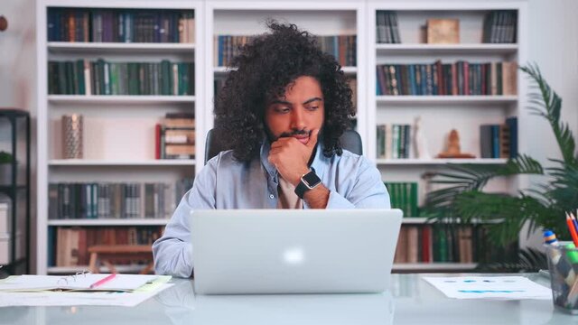 Focused young Arabian ethnic man professional thinking working with laptop makes puzzled expression face, doing career in technology or financial business sits at table in modern office.