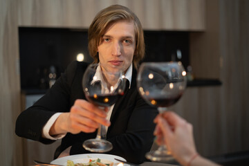 toast on a date glasses of red wine, dinner at home in the evening with alcohol, young man with a glass at home, valentines day couple in love, valentines day