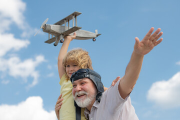 Old grandfather and young child grandson having fun with toy plane on sky. Child dreams of flying, happy childhood with granddad.