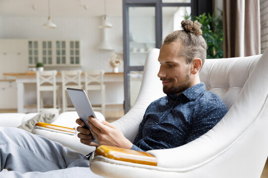 Smiling relaxed millennial gadget user man reading book on tablet computer screen, watching movie, virtual training webinar, using online app, browsing internet, social media, shopping