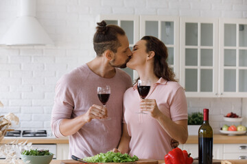 Happy sweet dating, married couple in love celebrating anniversary, birthday, special event, moving into new home, drinking red wine in kitchen, kissing on lips, cooking fresh salad for dinner