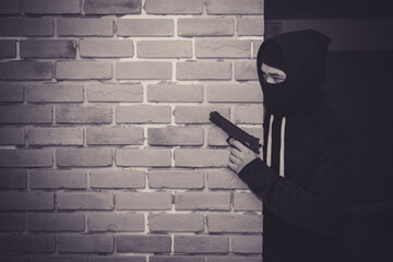 Thief wear cover faces and black jacket  with gun is hiding behind the old wall.