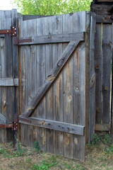 A slightly opened old wooden gate in the fence with a wooden latch. The gate in the fence is made of boards. Daylight. Summer.