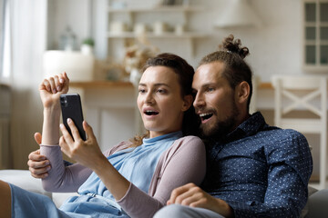 Excited surprised millennial dating couple getting unexpected news on smartphone, reading text message, staring at screen together with shocked amazed faces. Happy girl and guy using mobile phone