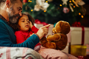 Adorable father and his daughter playing with teddy bear at home