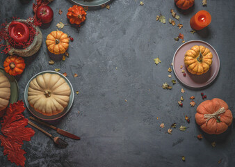 Autumn background with various orange pumpkins, candles, cutlery and autumn leaves on dark concrete kitchen table. Frame with copy space. Top view.