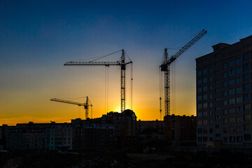 Big crane silhouette and many workers building new construction under a beautiful colorful sunset sky.Tall building under construction with scaffolds,Construction Site of New Building