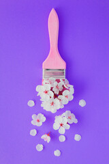 Paintbrush with white flowers on the purple background. Creative flowers composition.Top view.