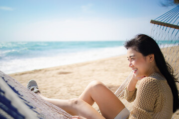 Smile Asian female relaxing sitting on hammock on sea beach