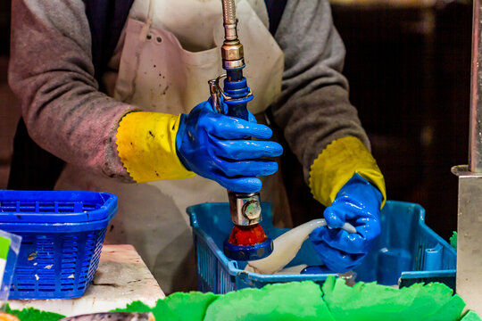 Unrecognizable fishmonger woman cleaning squid at the Boqueria market in Barcelona (Spain).