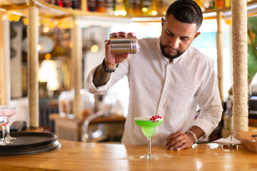 Young latin man carefully preparing an alcoholic drink in a modern cocktail bar. Space for text....