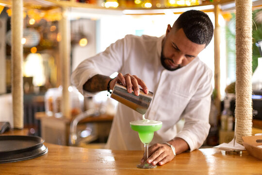 Elegant young Latin waiter delicately preparing an exotic drink. Space for text. Selective focus.