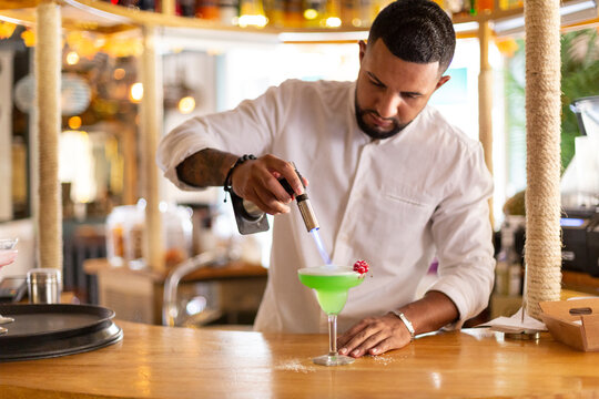 Elegant young Latin American waiter carefully preparing an alcoholic drink in a modern restaurant. Space for text. Selective focus.