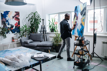 Talanted black man painting on an easel inside of his workshop in apartment