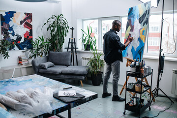 Gifted black man painting on an easel inside of his workshop in apartment