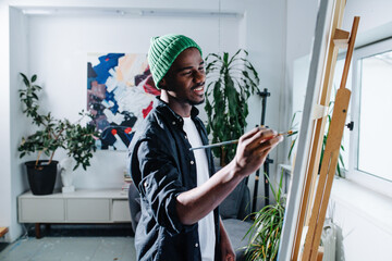 Inspired happy black man painting on an easel inside of his apartment - Powered by Adobe