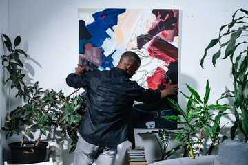 African american painter hanging his abstract colorful piece on the wall.