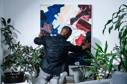 African American Painter Hanging His Abstract Colorful Piece On The Wall.