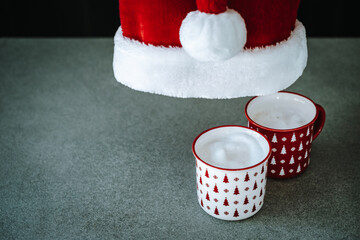 Obraz na płótnie Canvas Christmas background. Under Fluffy Santa's hat two cups of coffee cappuccino or latte. Mugs decorated with Xmas ornaments. Winter holidays concept.