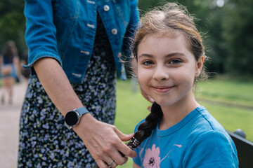 Close up portrait of a girl in braided hair smiling next to her mother in a park