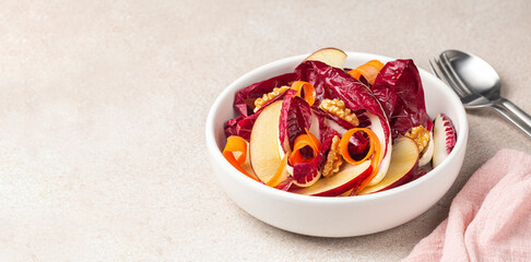 Close-up of radicchio, apple, walnut, carrot salad in a white bowl.  Healthy and vegan life concept. Beige table surface. Banner size. Copy space.