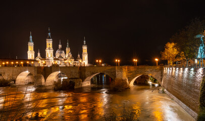 Obraz premium Long exposure at night on the Puente de Piedra next to the Basilica of Nuestra Señora del Pilar on the Ebro river in the city of Zaragoza, Aragon. Spain