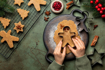Girls hands cooking Christmas cookies, gingerbread man with cutter. Made with hazelnut butter. Christmas and New Year traditions concept, view from above, green background with fir tree brunches.
