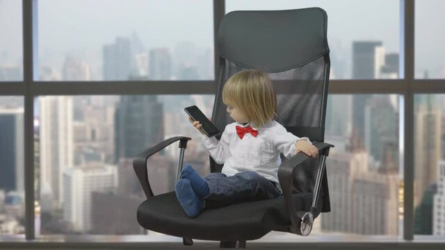 Little blond child sit on businessman chair talk at phone in office