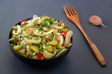 Slicing fermented green tomatoes and cucumbers with onions and pickled peppers in a black cup on a gray table