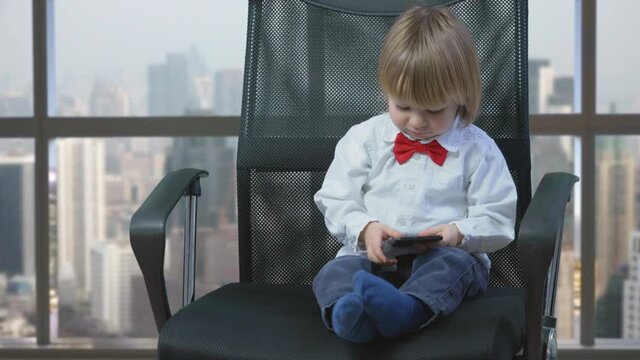 Portrait of little child sit on business chair look on phone and show thumb up