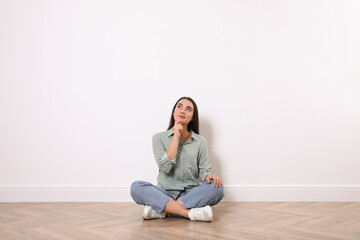 Fototapeta na wymiar Young woman sitting on floor near white wall indoors