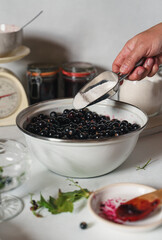 Woman's hands adding sugar to blackberries while making jam