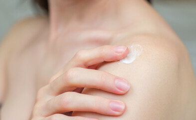 An unrecognizable woman applies moisturizer to her shoulder. Skin care