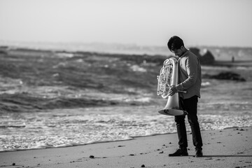 Male musician with a tuba near the ocean. Black and white photo. Black and white photo.