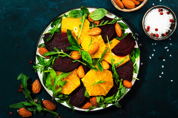 Beet Salad with orange, arugula and almonds on blue table background. Vegan healthy food. Copy space