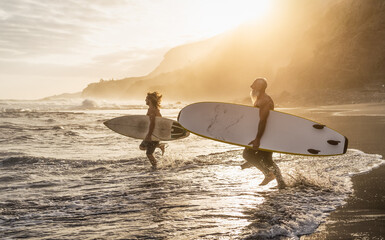 Happy fit friends surfing together on tropical beach at sunset time - People lifestyle and extreme...